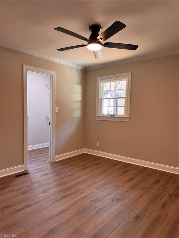 empty room featuring dark wood-type flooring, crown molding, and baseboards