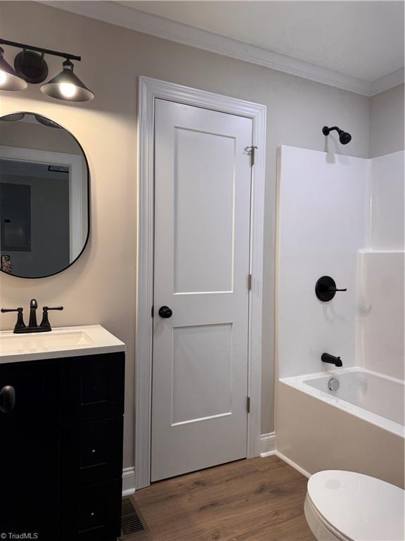 full bathroom with toilet, wood finished floors, vanity, bathing tub / shower combination, and crown molding