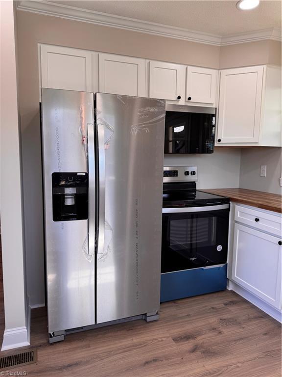 kitchen with stainless steel appliances, ornamental molding, wood finished floors, and white cabinets