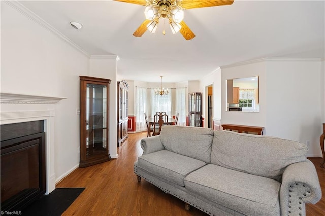 living room with a fireplace with flush hearth, wood finished floors, baseboards, ceiling fan with notable chandelier, and ornamental molding