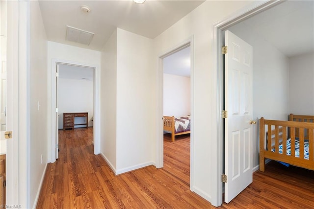 hallway with baseboards, an upstairs landing, visible vents, and light wood-style floors