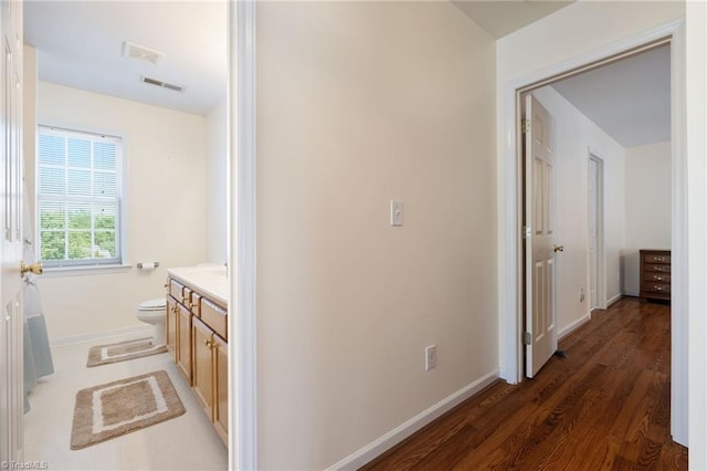hall with baseboards, wood finished floors, and visible vents