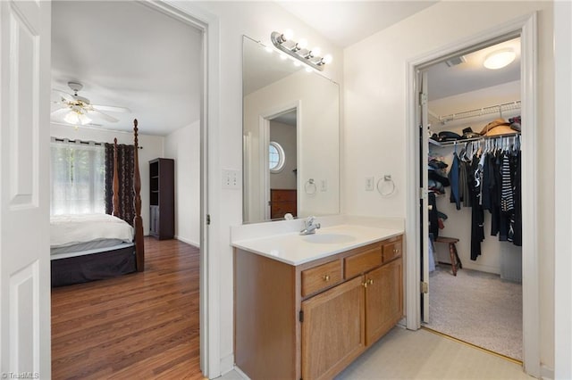 ensuite bathroom featuring vanity, wood finished floors, ceiling fan, a spacious closet, and ensuite bath