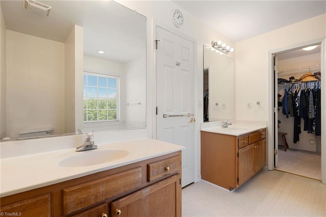 full bathroom featuring visible vents, a sink, a walk in closet, and two vanities