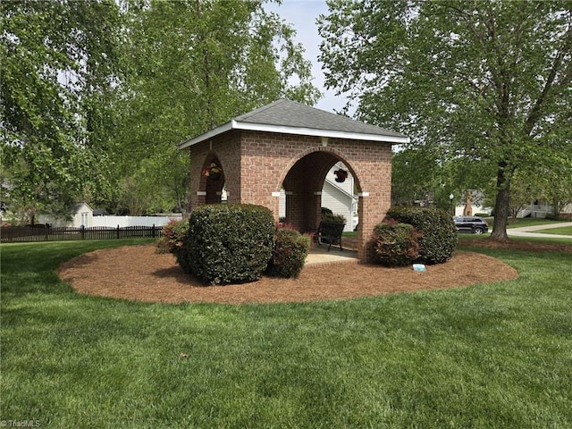 exterior space featuring brick siding, a shingled roof, fence, and a yard