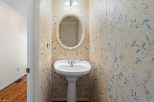 bathroom featuring crown molding, wallpapered walls, visible vents, and wood finished floors