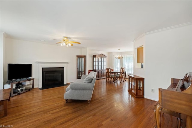 living area with a fireplace with flush hearth, ornamental molding, wood finished floors, and ceiling fan with notable chandelier