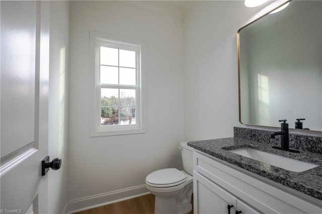 half bathroom with toilet, vanity, baseboards, and wood finished floors