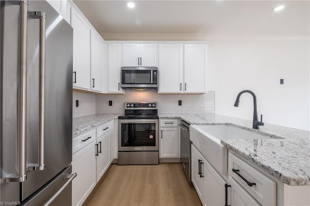 kitchen with light wood-style flooring, a sink, decorative backsplash, stainless steel appliances, and white cabinets