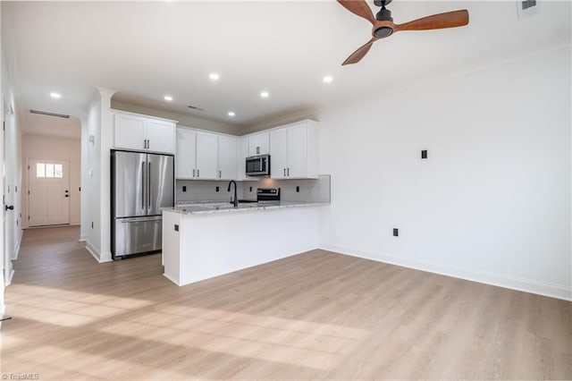 kitchen with a peninsula, ceiling fan, appliances with stainless steel finishes, light wood-type flooring, and backsplash