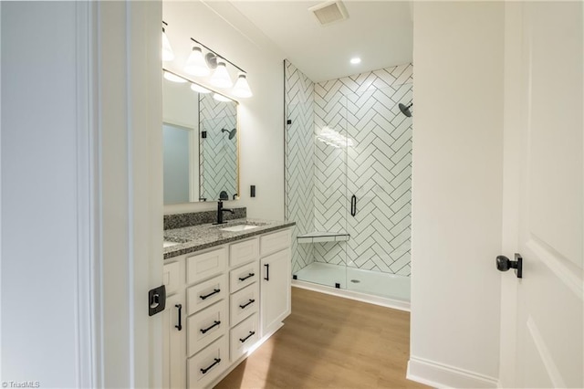 bathroom featuring visible vents, a shower stall, double vanity, wood finished floors, and a sink