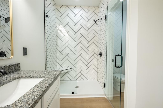 bathroom with toilet, a stall shower, vanity, and wood finished floors