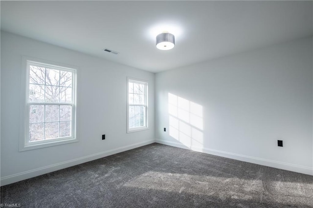 spare room featuring baseboards, visible vents, and dark carpet