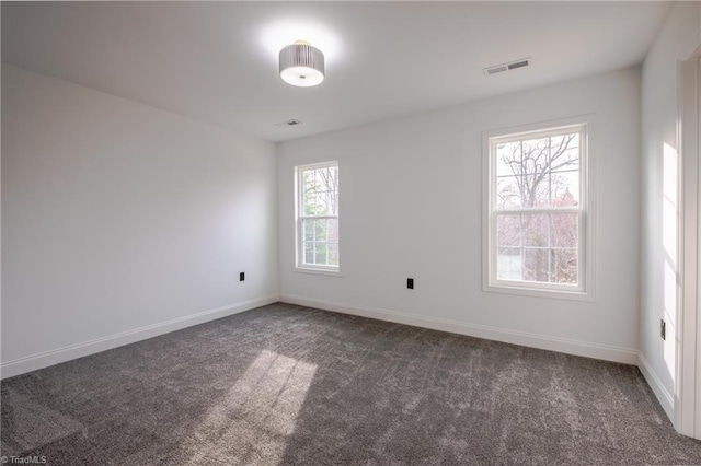 empty room featuring baseboards, visible vents, and dark colored carpet