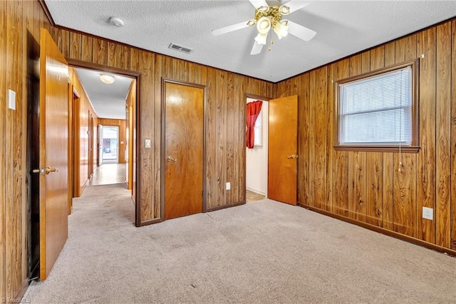 unfurnished bedroom featuring ceiling fan, wooden walls, a textured ceiling, light colored carpet, and a closet