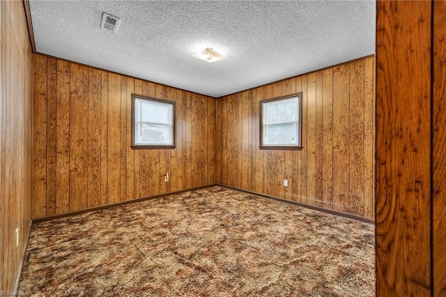 carpeted spare room with wooden walls and a textured ceiling