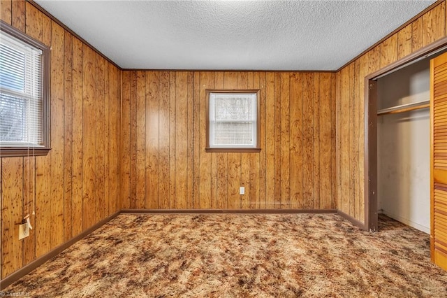 unfurnished bedroom with wooden walls, a closet, a textured ceiling, and carpet