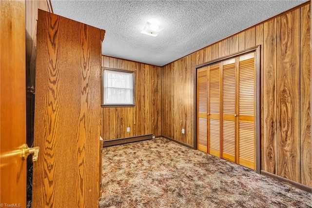 unfurnished bedroom with a baseboard heating unit, wooden walls, a textured ceiling, light colored carpet, and a closet