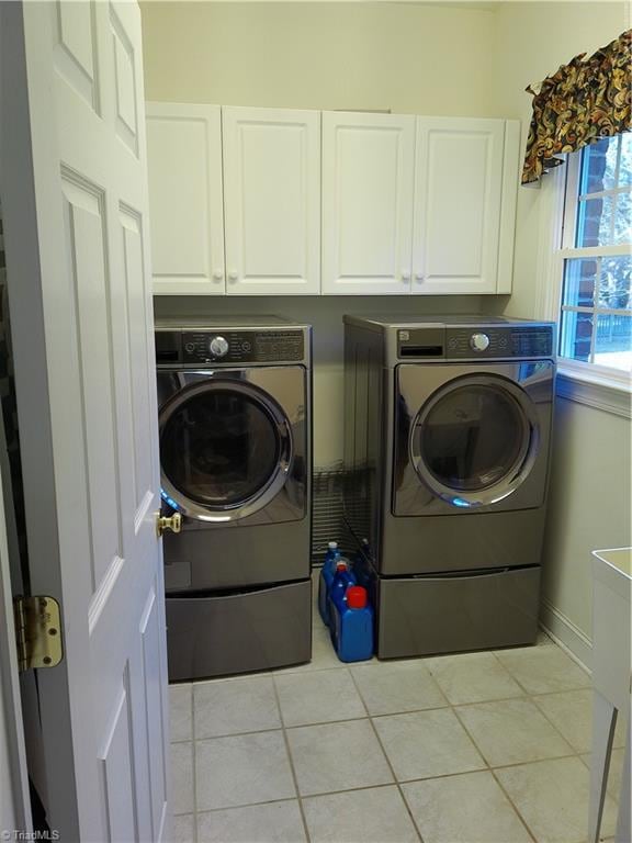 clothes washing area with washer and clothes dryer, cabinets, and light tile patterned floors