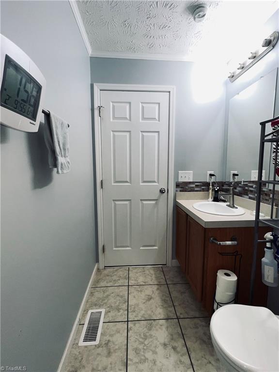 bathroom featuring vanity, toilet, crown molding, tile patterned floors, and a textured ceiling