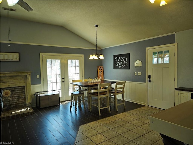 dining space featuring visible vents, lofted ceiling, a wainscoted wall, french doors, and a fireplace