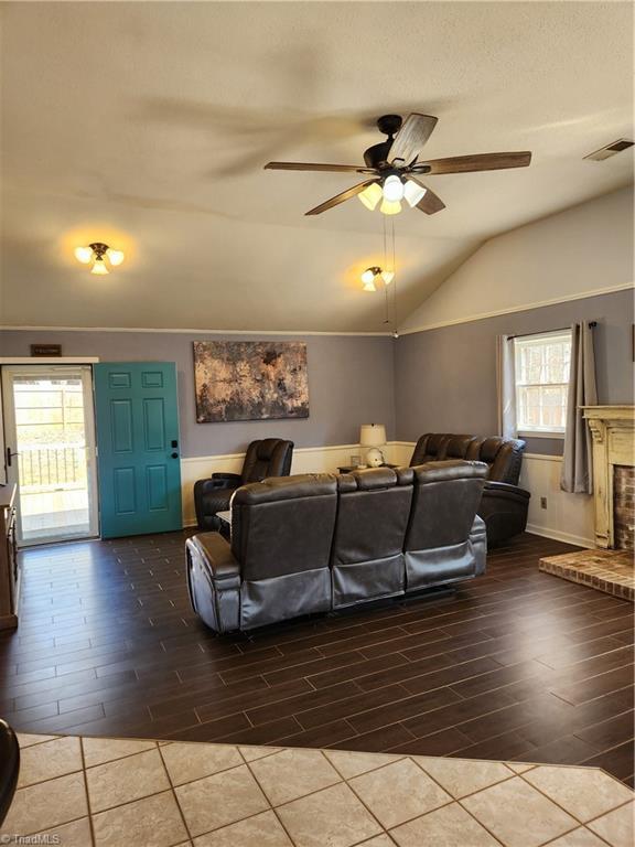 living area with vaulted ceiling, a brick fireplace, wood finished floors, and visible vents