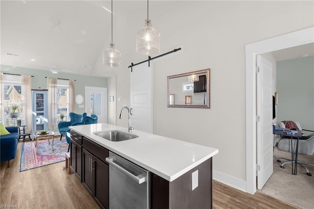 kitchen with a barn door, a sink, light countertops, hanging light fixtures, and dishwasher