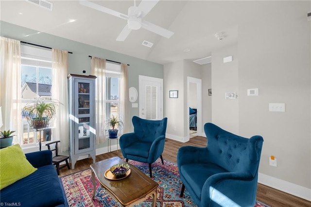 living area featuring visible vents, a ceiling fan, vaulted ceiling, wood finished floors, and baseboards