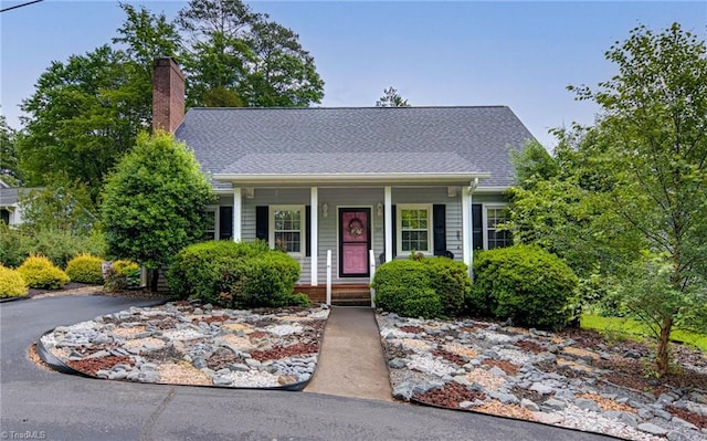 view of front of house with covered porch, a chimney, and a shingled roof