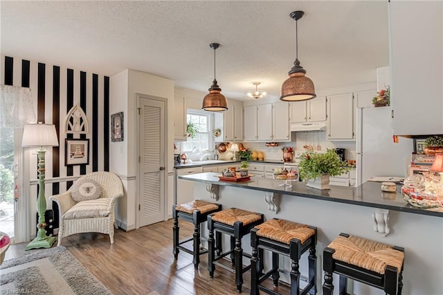 kitchen featuring under cabinet range hood, a peninsula, freestanding refrigerator, dark countertops, and light wood-style floors