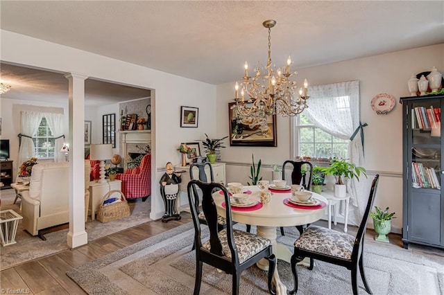 dining space featuring wood finished floors, a chandelier, and decorative columns
