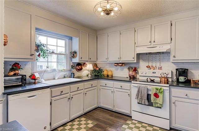 kitchen featuring white appliances, under cabinet range hood, a sink, dark countertops, and decorative backsplash