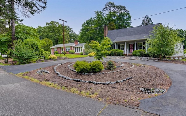 single story home with curved driveway, a chimney, and covered porch