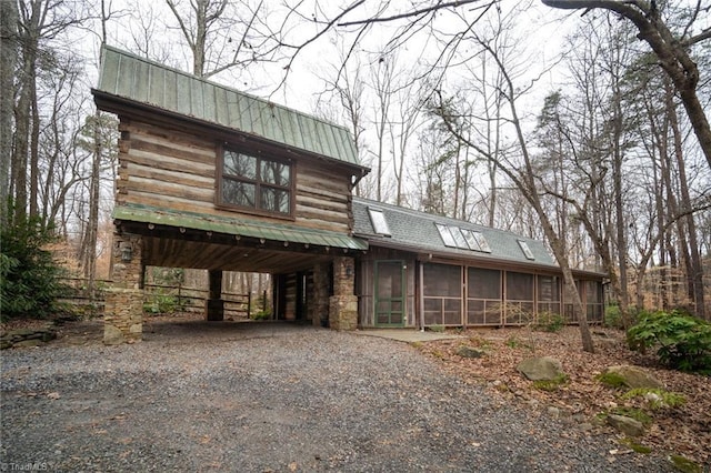 cabin featuring metal roof, a sunroom, stone siding, a carport, and gravel driveway