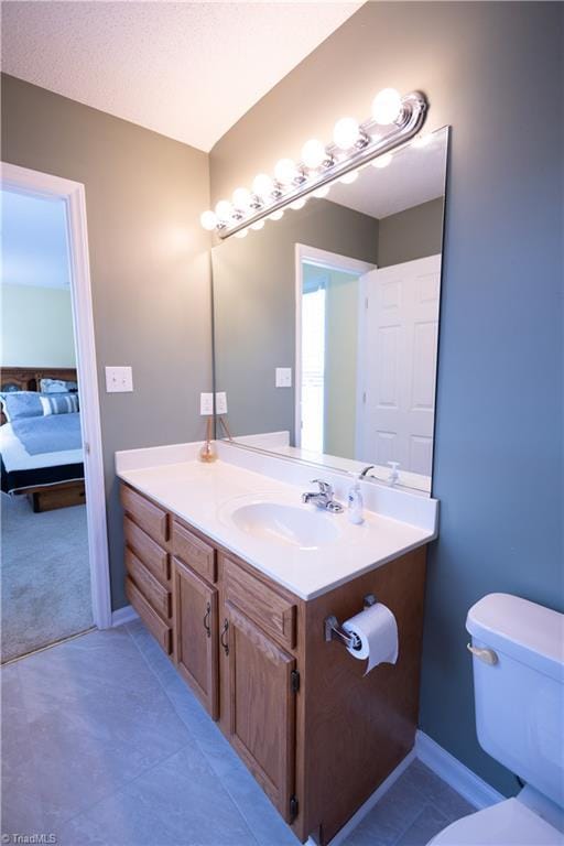 ensuite bathroom featuring toilet, vanity, baseboards, and tile patterned floors