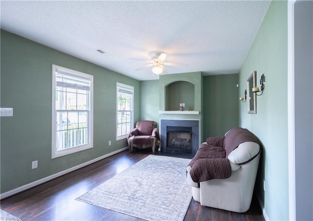 sitting room with a textured ceiling, a fireplace, dark wood-style floors, baseboards, and a ceiling fan