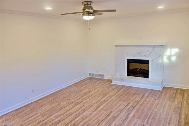 unfurnished living room with ceiling fan, ornamental molding, a premium fireplace, and light hardwood / wood-style flooring