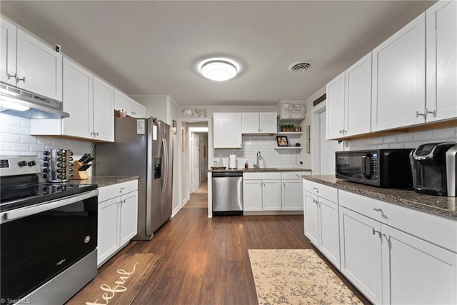 kitchen with dark stone counters, appliances with stainless steel finishes, tasteful backsplash, dark hardwood / wood-style flooring, and white cabinetry