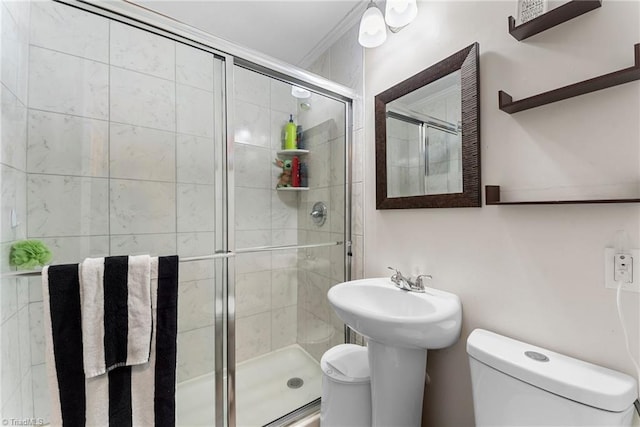 bathroom with a shower with shower door, toilet, ornamental molding, and sink