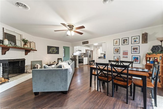 living room with ceiling fan, dark hardwood / wood-style flooring, crown molding, and a brick fireplace