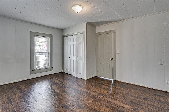 unfurnished bedroom featuring ornamental molding, dark wood-style flooring, a closet, and baseboards