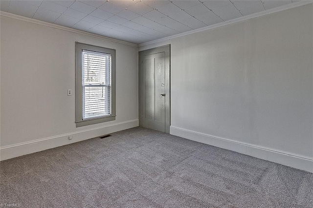 spare room with carpet floors, visible vents, crown molding, and baseboards