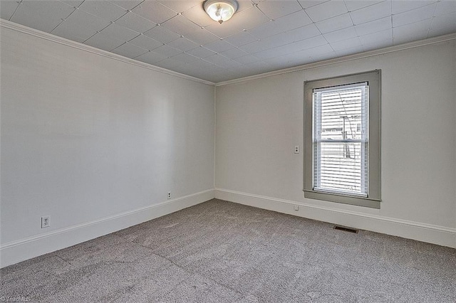 carpeted spare room featuring baseboards, visible vents, and crown molding