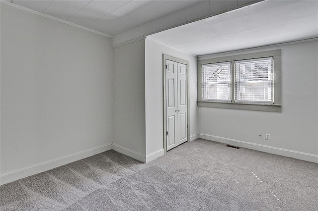 unfurnished bedroom featuring carpet floors, visible vents, baseboards, ornamental molding, and a closet