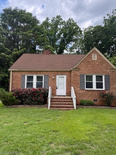 view of front facade with entry steps, brick siding, a front lawn, and a chimney