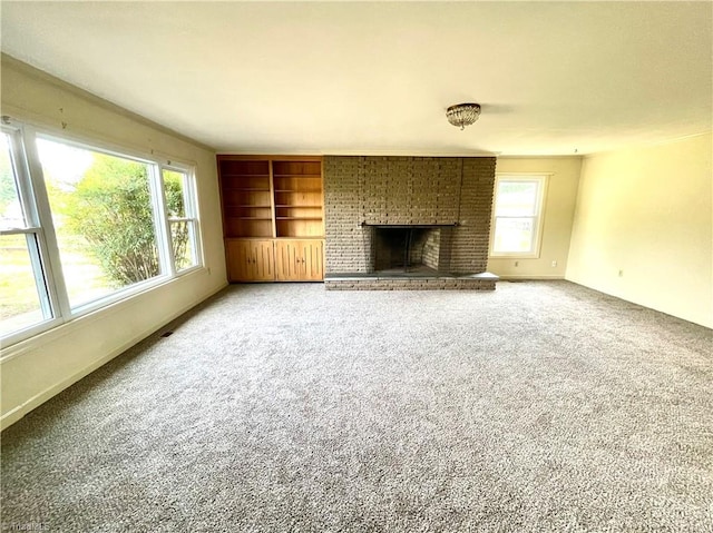 unfurnished living room with carpet flooring, built in shelves, a brick fireplace, and brick wall