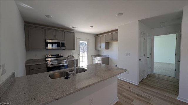 kitchen featuring kitchen peninsula, appliances with stainless steel finishes, light stone counters, sink, and light hardwood / wood-style flooring