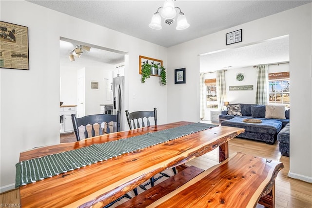 dining area featuring light wood-style floors, a notable chandelier, a textured ceiling, and baseboards