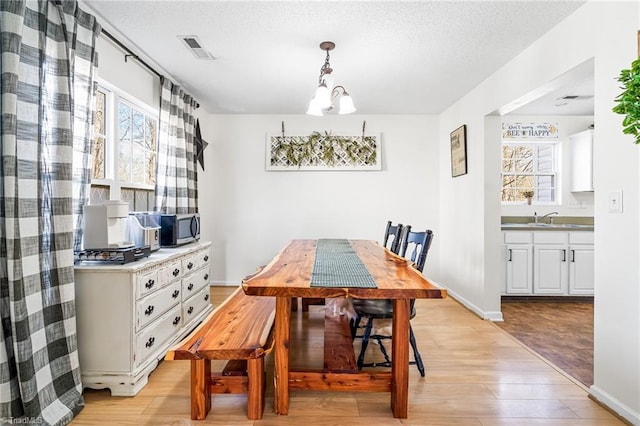 dining room featuring light wood finished floors, visible vents, a textured ceiling, a chandelier, and baseboards