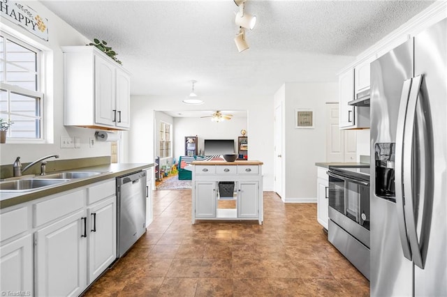 kitchen with stainless steel appliances, white cabinets, a sink, a textured ceiling, and under cabinet range hood